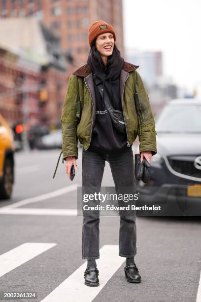 Aymeline Valade wears a brown ribbed wool beanie hat, a black hoodie sweater , a green bomber jacket , black denim jeans pants , black pointed shoes...