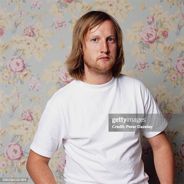 man wearing white t-shirt standing by floral-papered wall, portrait - t shirt stockfoto's en -beelden