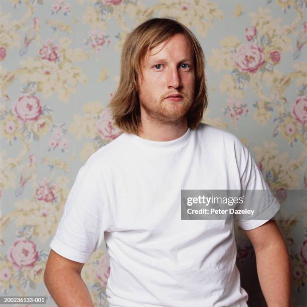 man wearing white t-shirt standing by floral-papered wall, portrait - t shirt stock pictures, royalty-free photos & images