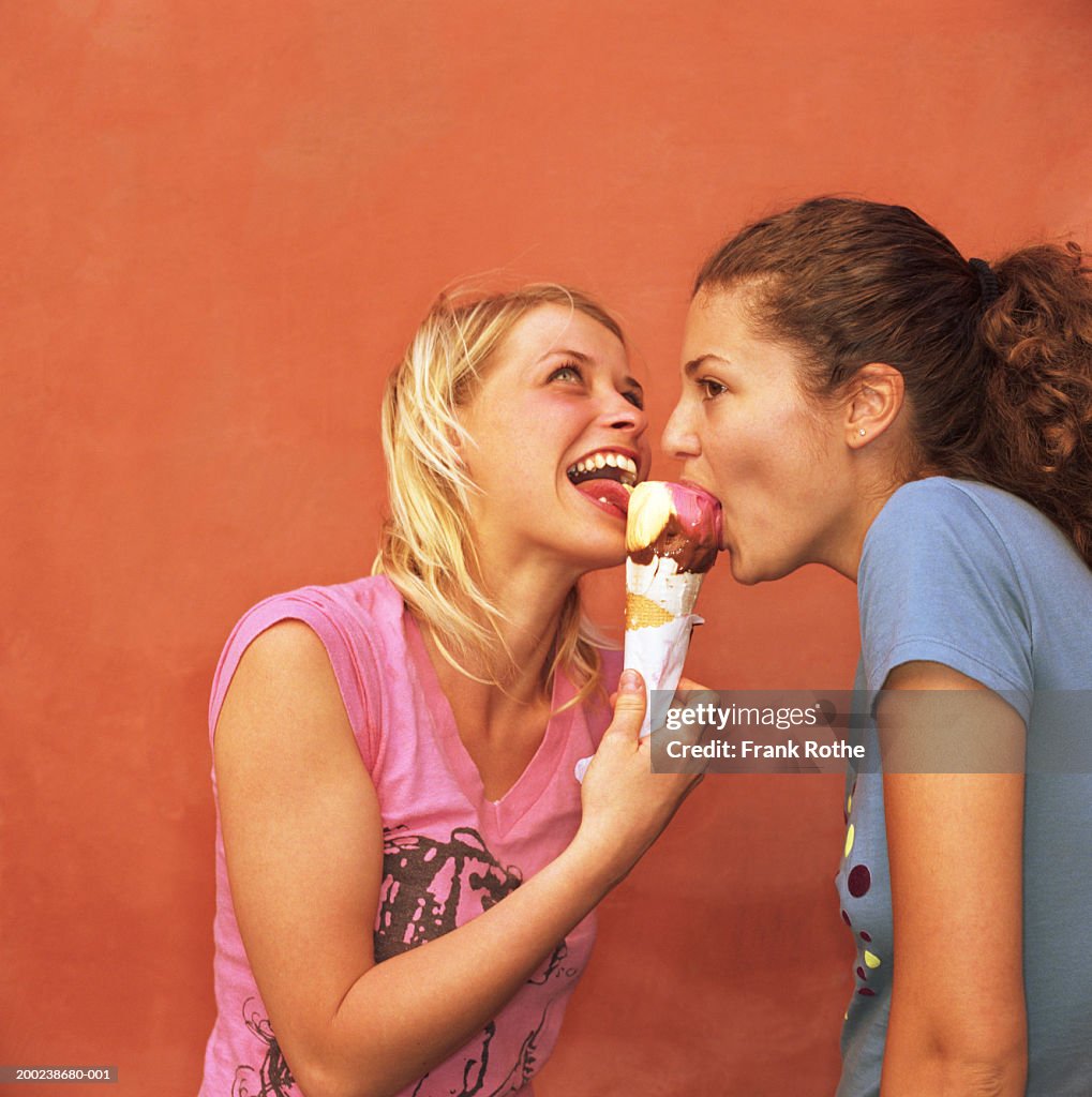 Two young friends sharing ice cream cone, close-up