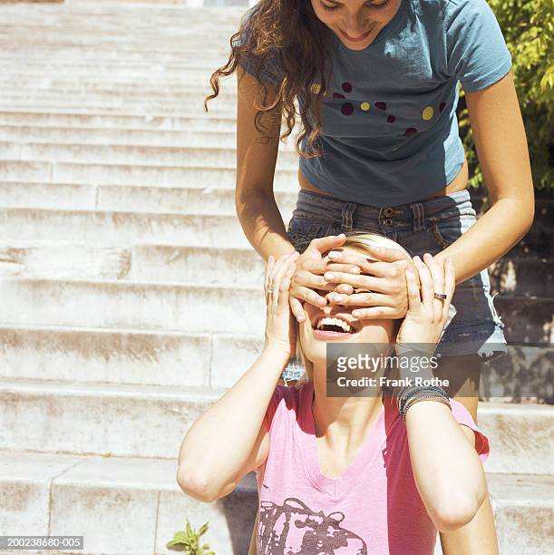 young woman with hands covering friend's eyes, smiling - friends greeting stock pictures, royalty-free photos & images