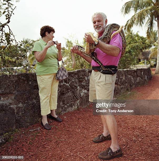 mature man holding snakes, mature woman with camera in background - snakes beard stock pictures, royalty-free photos & images