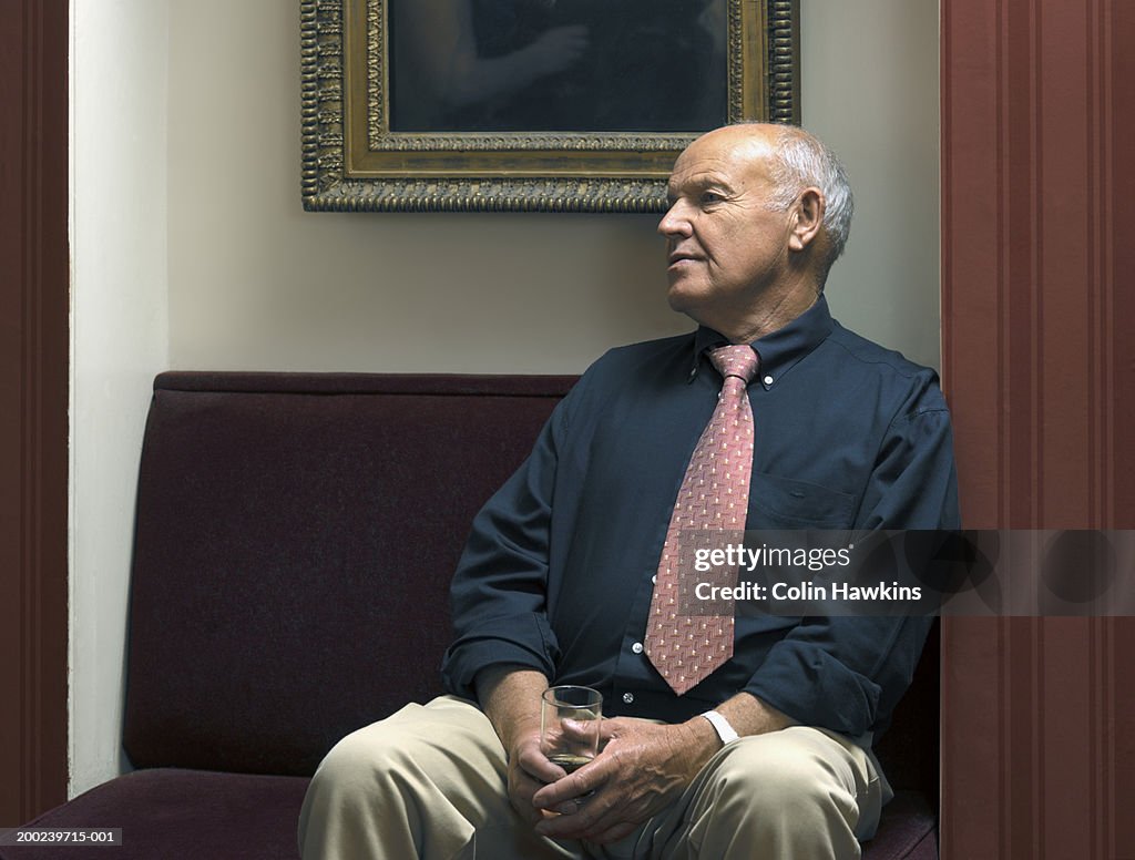 Senior man seated in theatre foyer, holding wine glass