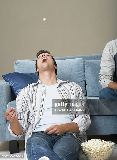 young man by sofa, tossing popcorn in air, head back and mouth open - throwing food stock pictures, royalty-free photos & images