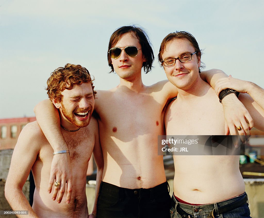 Three barechested young men embracing on rooftop, portrait