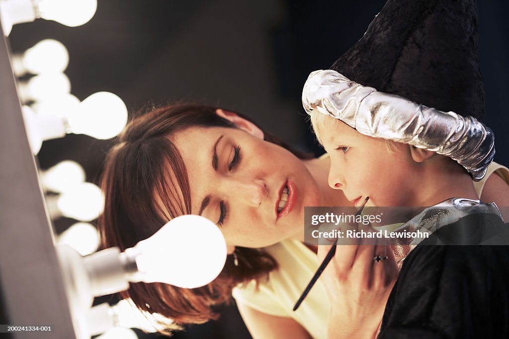 Teacher applying make-up to boy (3-5) in wizard costume backstage