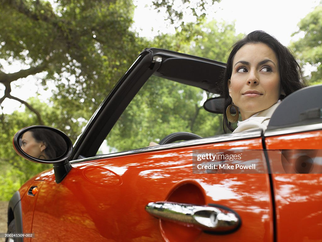 Young woman in red convertible car, looking over shoulder