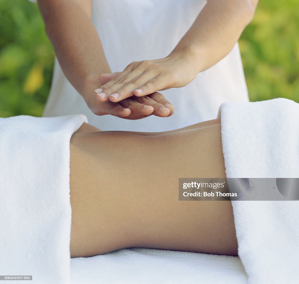 Female therapist performing Reiki holding hands over woman's stomach