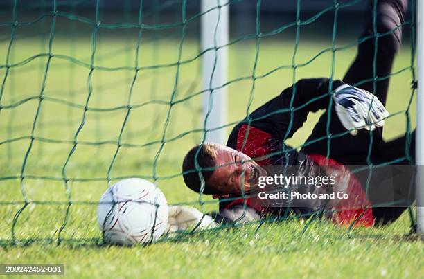 male football goalie lying on field, reaching for ball - amateur stock-fotos und bilder