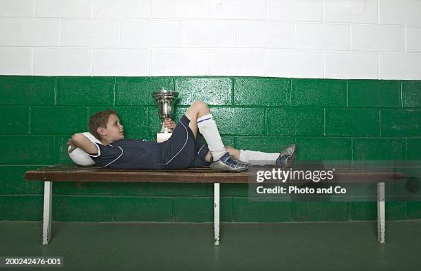 boy (8-10) lying on bench in change room, holding trophy - soccer bench stock pictures, royalty-free photos & images