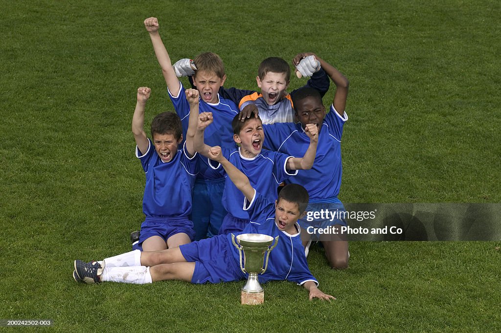 Football team of boys (8-12) celebrating in field by trophy, portrait