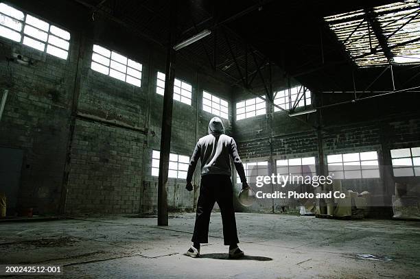 man wearing hooded jacket, holding football in warehouse, rear view - man and his hoodie imagens e fotografias de stock