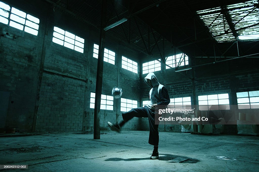 Man wearing hooded jacket, holding football in warehouse, side view