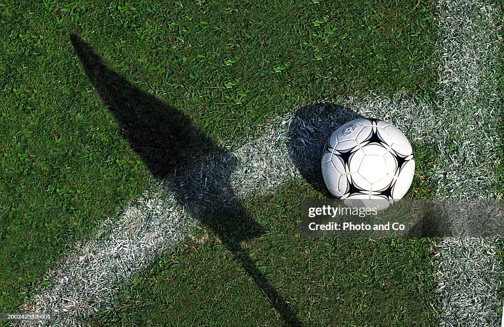 Football on grass by pitch marking and shadow of flag