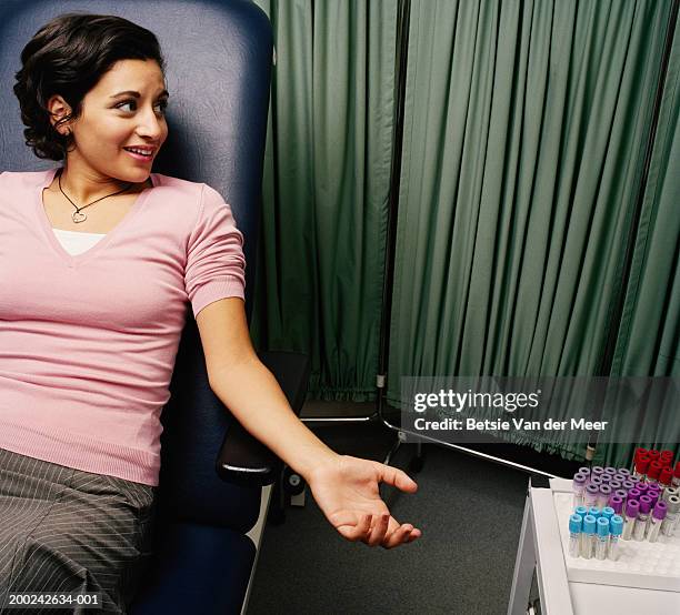 young woman holding out arm by sample containers - blood donation imagens e fotografias de stock
