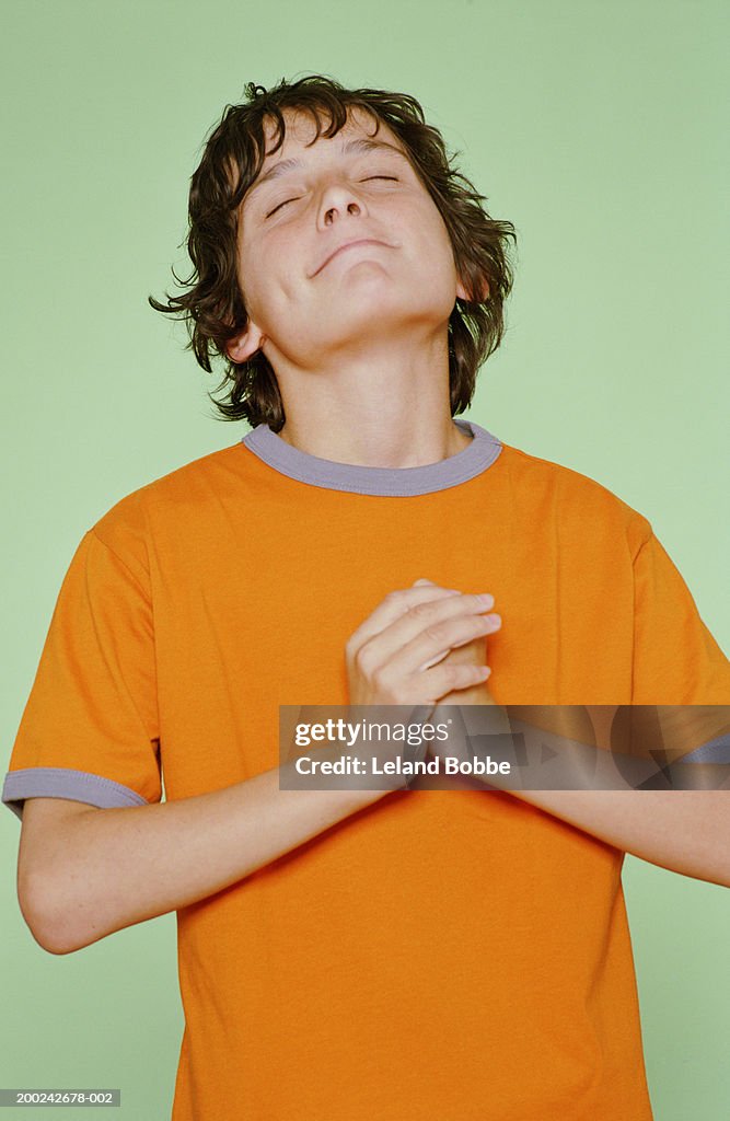 Boy (10-12) with hands together and eyes closed