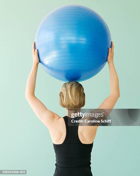 young woman holding exercise ball above head, rear view - pilates ball man stock-fotos und bilder