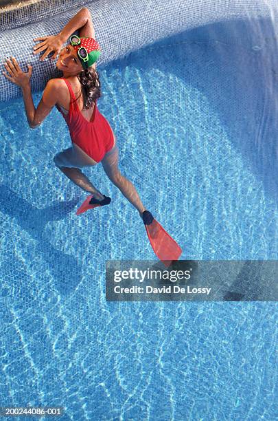 young woman, wearing swimming cap, goggles and flippers, in swimming pool, smiling, portrait - schwimmflosse stock-fotos und bilder