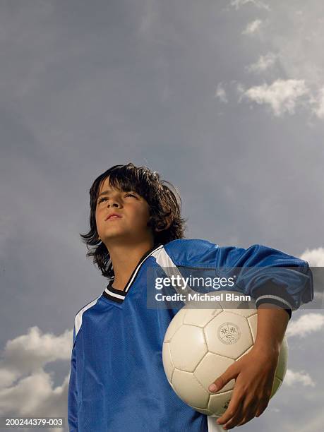 boy (8-10) footballer holding ball under arm, low angle view - sous le bras photos et images de collection