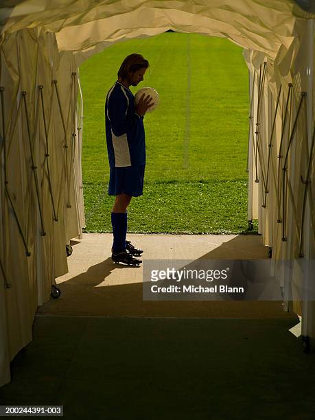 male footballer in tunnel leading to pitch, staring at ball, side view - football player tunnel stock pictures, royalty-free photos & images