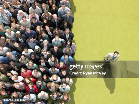 Young man standing to side of large crowd looking up, overhead view Young man standing to side of large crowd looking up, overhead view