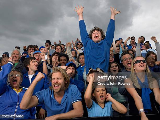 stadium crowd cheering, one man jumping high, low angle view - tribüne stock-fotos und bilder