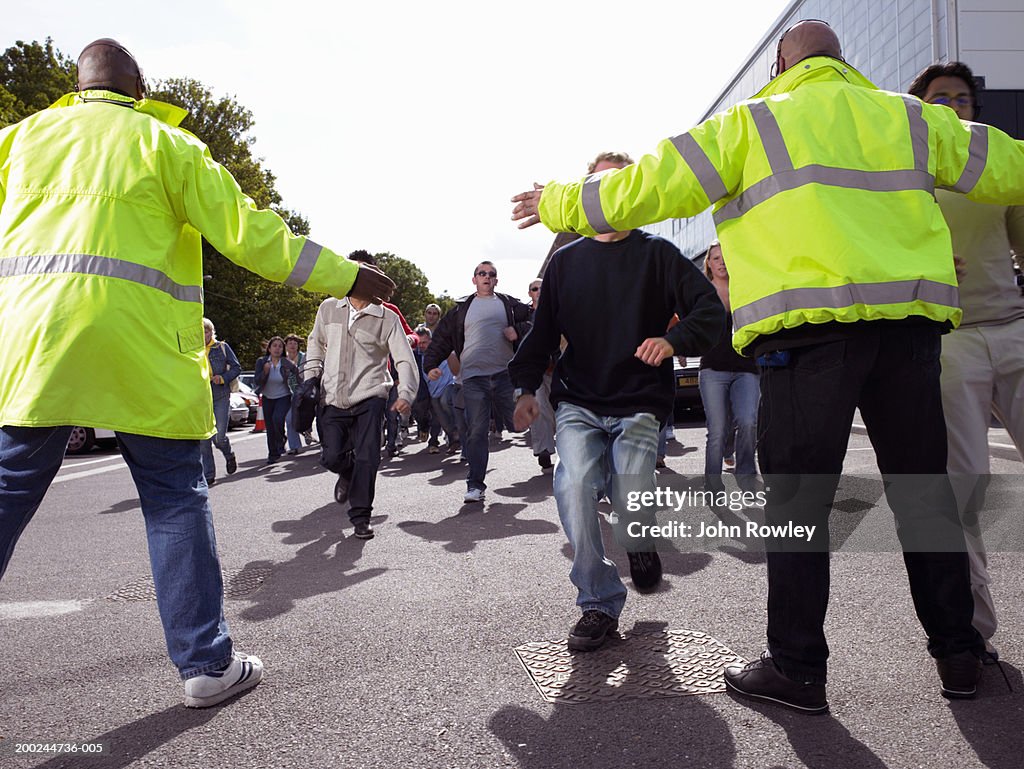 Two security guards holding out arms to stop advancing crowd