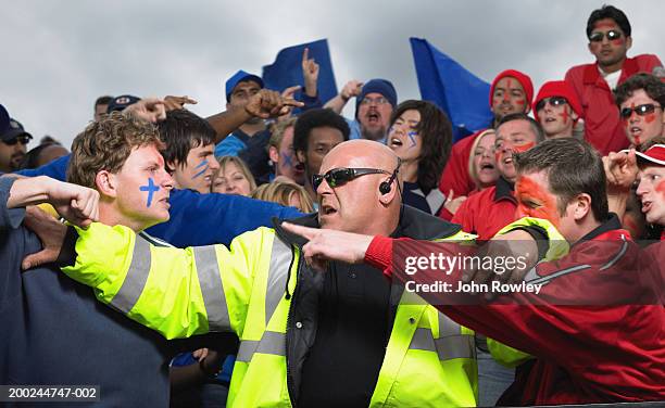 security guard trying to separate two fans in stadium crowd, close-up - rivalidad fotografías e imágenes de stock