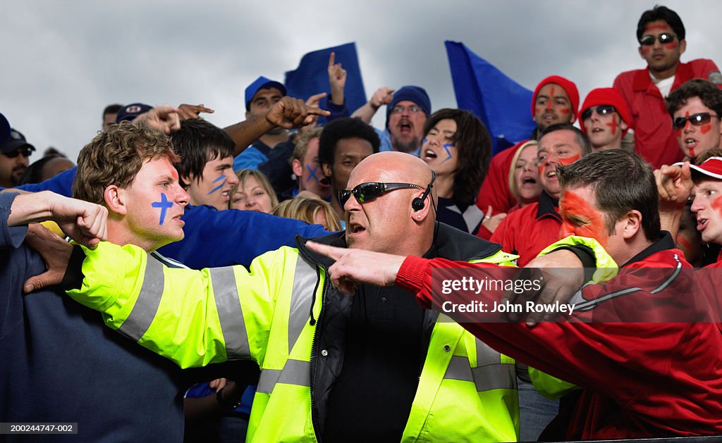 Security guard trying to separate two fans in stadium crowd, close-up