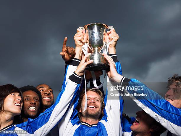 footballer player raising trophy cup, surrounded by team, close-up - fußballtrikot stock-fotos und bilder
