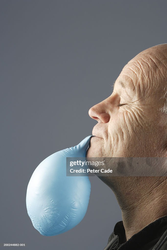 Mature man with baloon hanging from mouth, eyes closed, profile