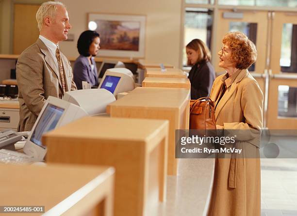 woman talking with bank teller at reception desk, side view - banque accueil photos et images de collection