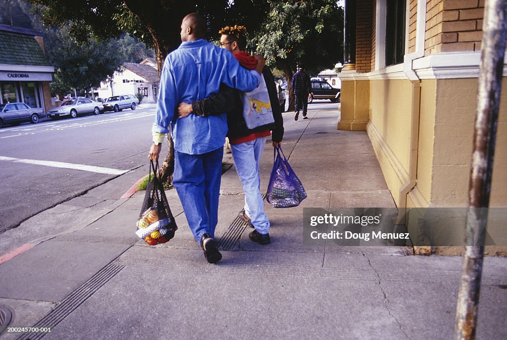 Gay couple walking home with groceries, (rear view)