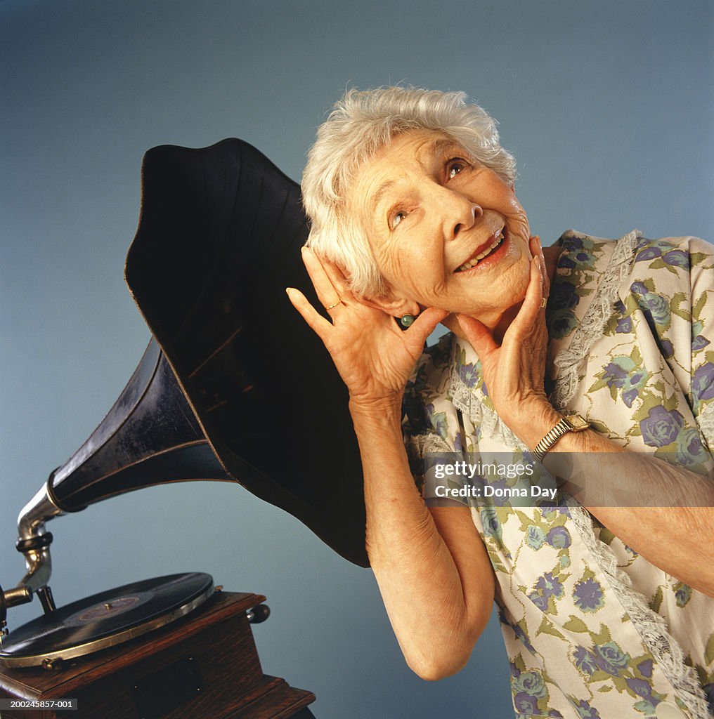 Senior woman listening to music from gramophone