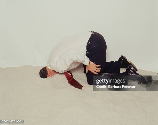 businessman hiding head in sand, side view - bury fotografías e imágenes de stock