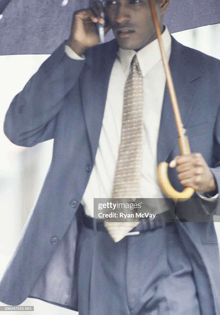 Businessman walking in rain, talking on cellular phone