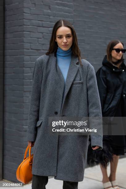 Model wears grey coat, orange bag outside Proenza Schouler on February 10, 2024 in New York City.