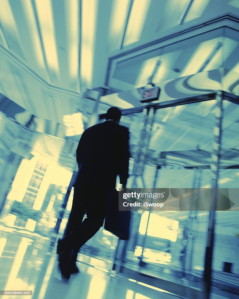 Businessman with suitcase walking into building, blurred motion