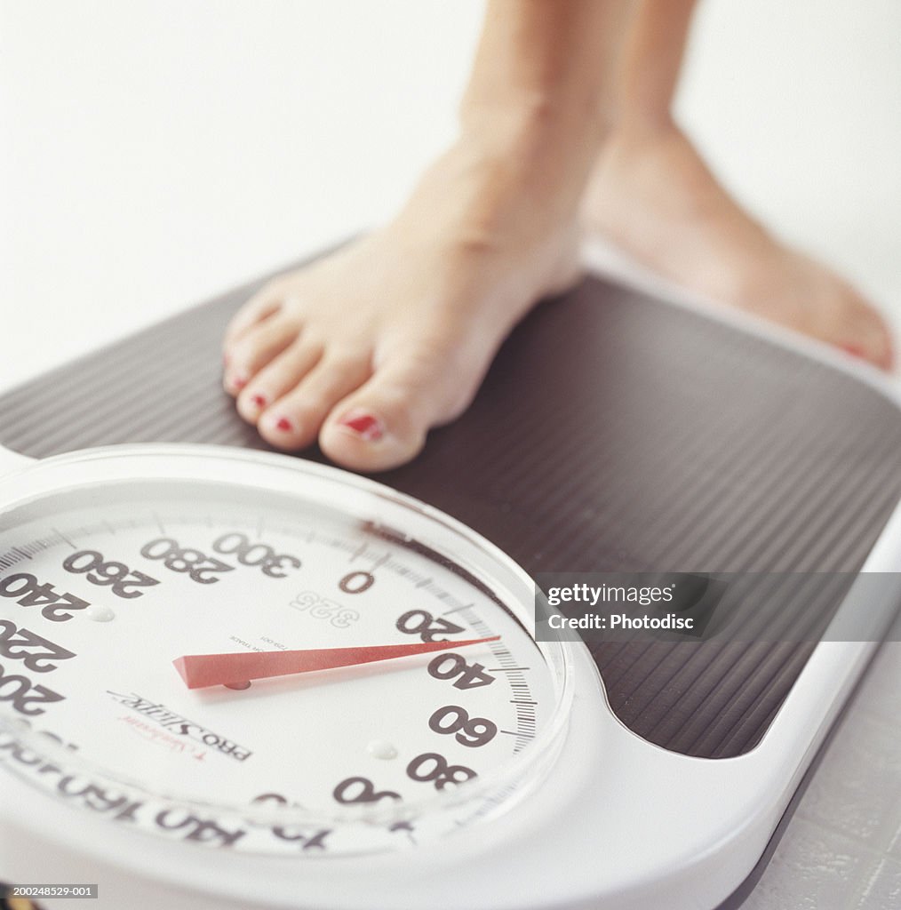 Woman stepping on bathroom scale, low section, Close-up of foot