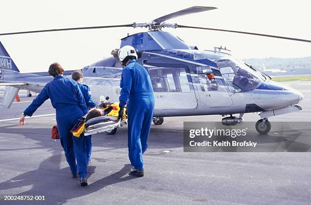 nurses and pilot carrying patient on stretcher to helicopter - ambulancia aérea fotografías e imágenes de stock