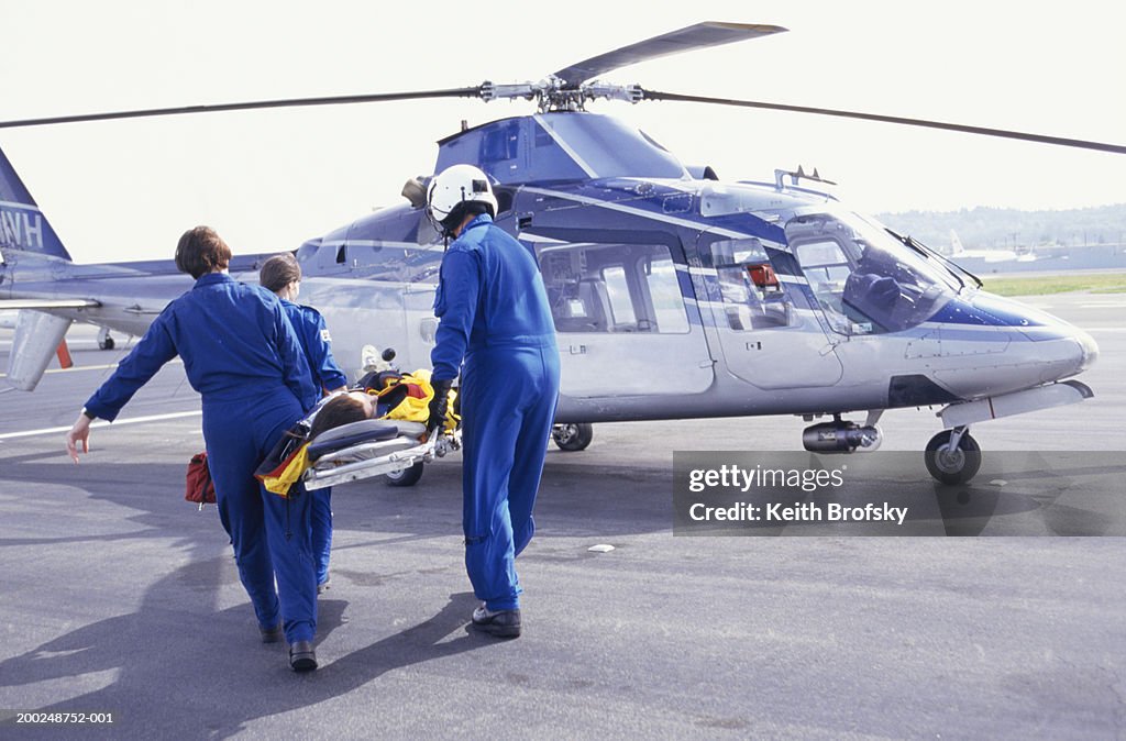 Nurses and pilot carrying patient on stretcher to helicopter