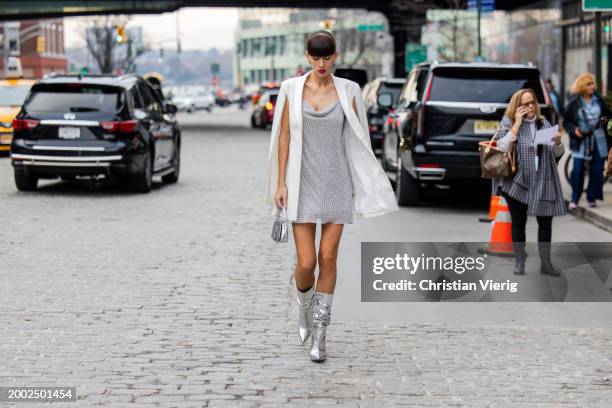 Katya Tolstova wears white cape, grey dress, silver bag, boots outside Alice + Olivia on February 10, 2024 in New York City.