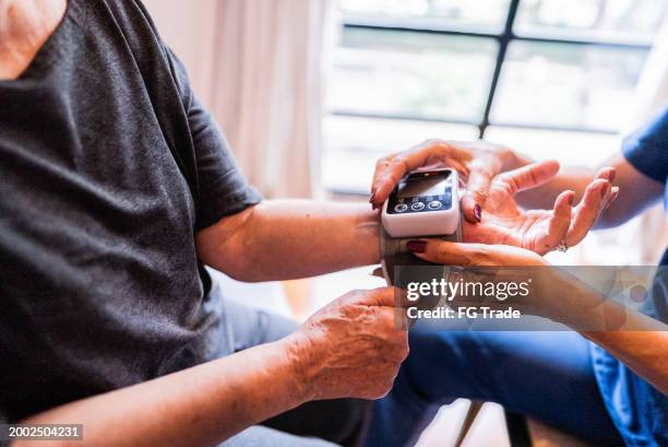close-up of nurse's hand taking blood pressure of a patient at home - hospital equipment stock pictures, royalty-free photos & images