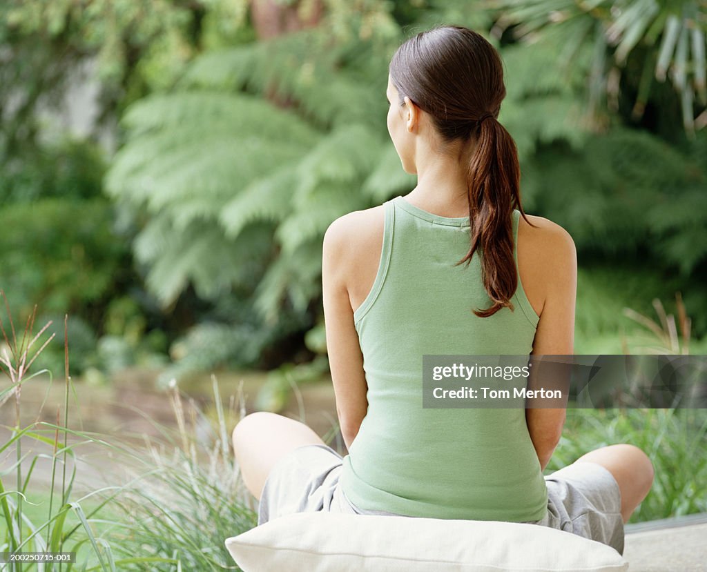 Woman sitting crossed legged on cushion, outdoors, rear view