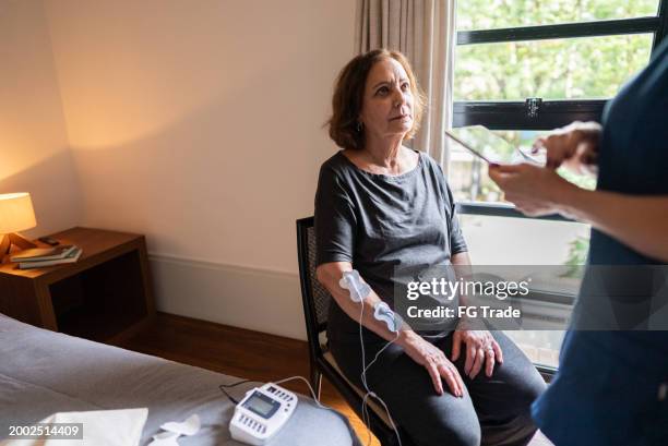 mujer mayor haciendo electroterapia en casa - sistema nervioso periférico fotografías e imágenes de stock