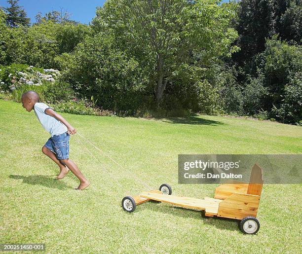 boy (5-7) pulling go-cart up hill in garden, side view - soapbox cart stock pictures, royalty-free photos & images