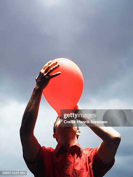 man blowing up red balloon - inflate stockfoto's en -beelden