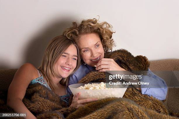 mother and daughter (13-15) on sofa sharing popcorn, laughing - teenagers eating with mum stock-fotos und bilder