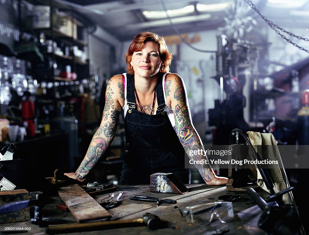 Woman with tattoos in both arms in factory, portrait