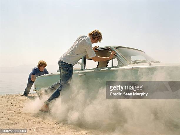 young men pushing car stuck in sand - mann schiebt stock-fotos und bilder